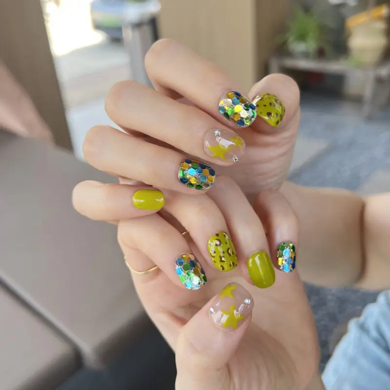Hand with colorful nail art featuring sequins and star designs.