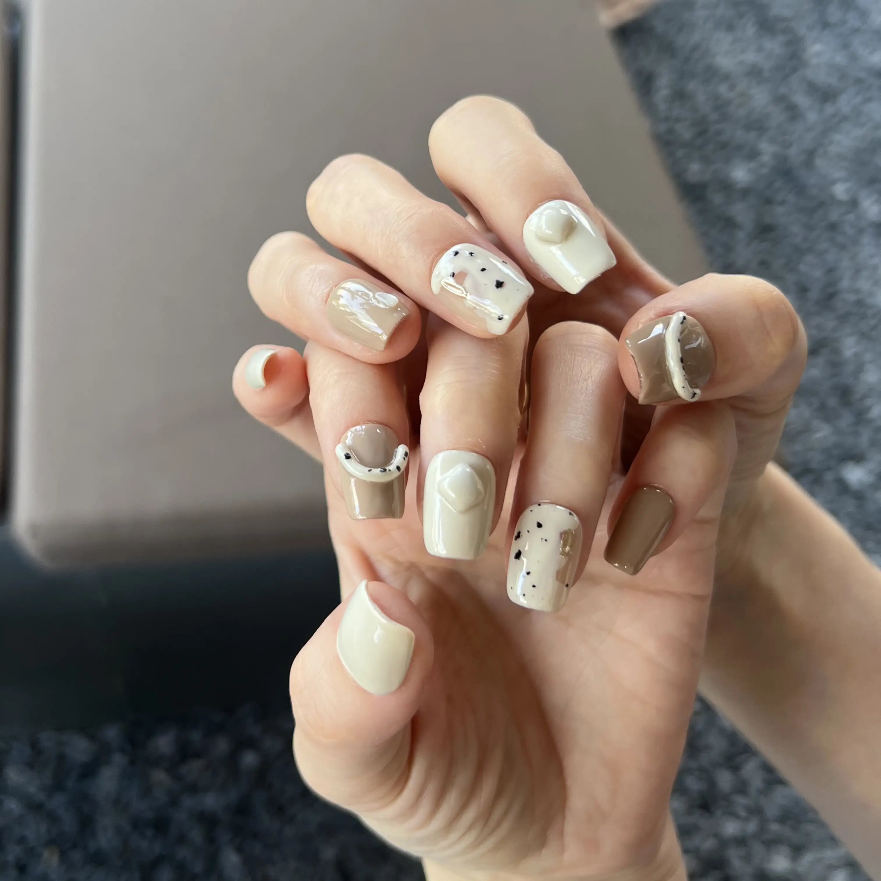 A set of nude and cream press on nails with 3D curved accents and speckled designs, displayed in a wooden tray.