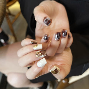 A set of press on nails in marble mocha, creamy white, and gold foil, featuring cable-knit texture and glossy finish, displayed on a card.
