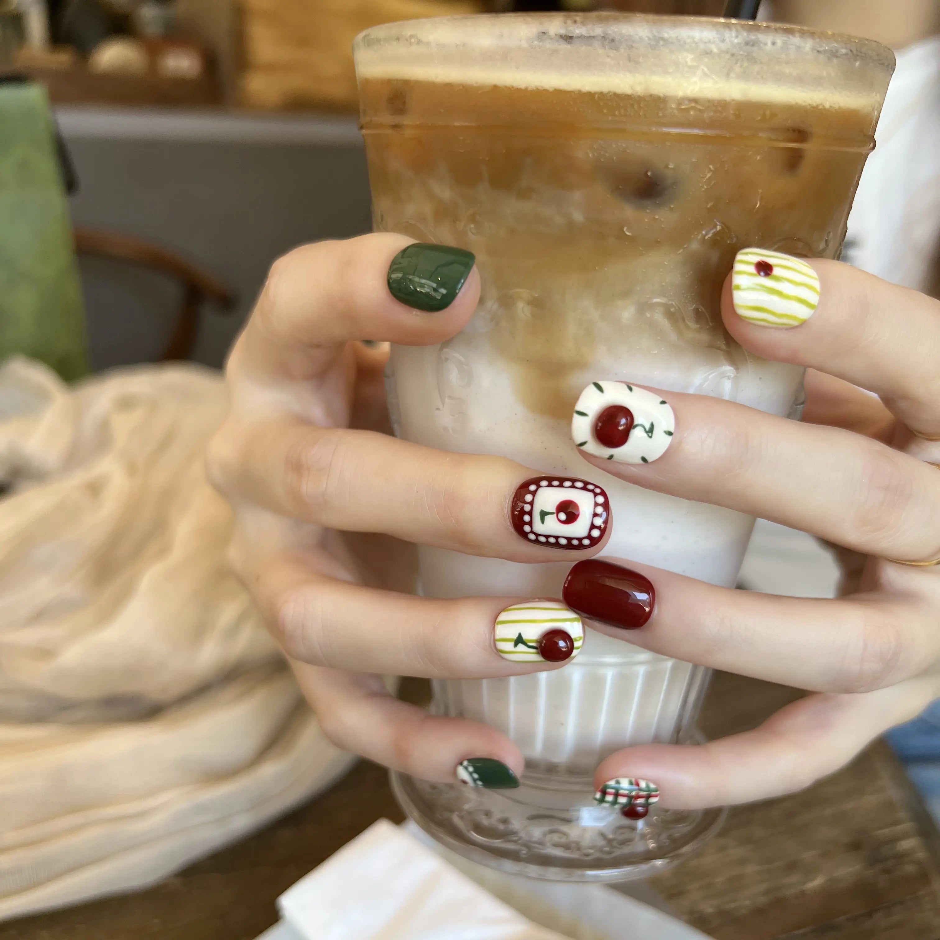 Hand holding a cup of iced coffee with decorated nails in a casual setting