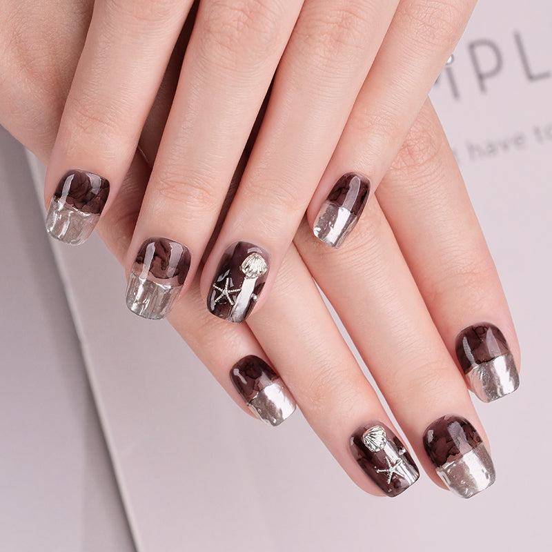 Close-up of hands with brown and silver nail design on a light background