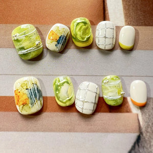 Hands with press on nails in green, white, and yellow, featuring abstract marble swirls, 3D accents, and modern grid line designs.
