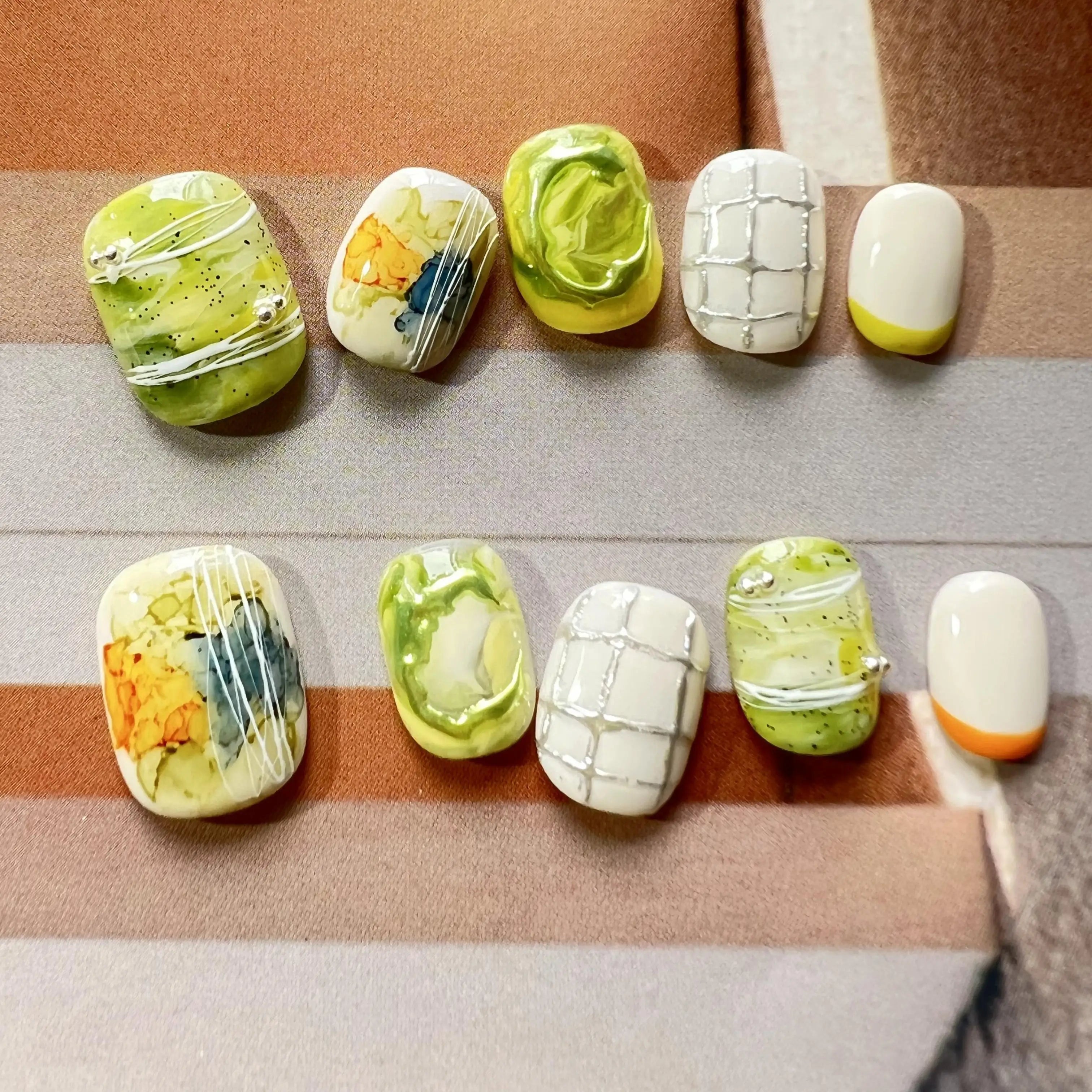 Hands with press on nails in green, white, and yellow, featuring abstract marble swirls, 3D accents, and modern grid line designs.