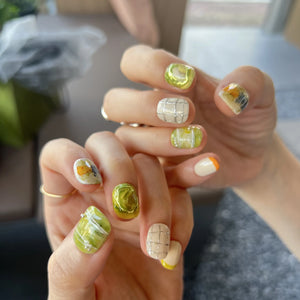 Hands with press on nails in green, white, and yellow, featuring abstract marble swirls, 3D accents, and modern grid line designs.
