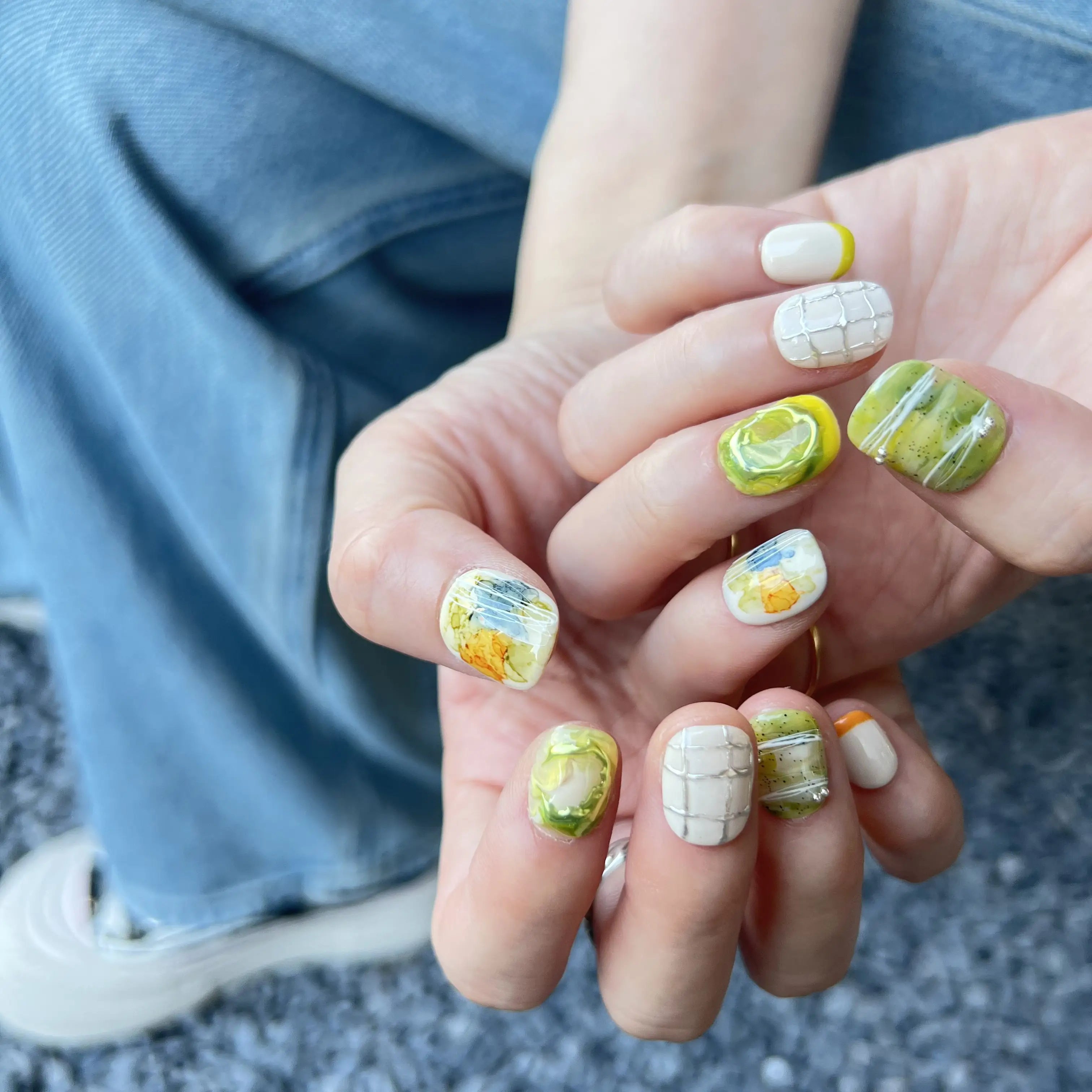 Hands with press on nails in green, white, and yellow, featuring abstract marble swirls, 3D accents, and modern grid line designs.