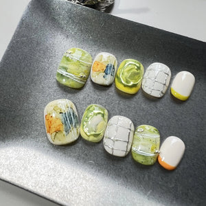 Hands with press on nails in green, white, and yellow, featuring abstract marble swirls, 3D accents, and modern grid line designs.