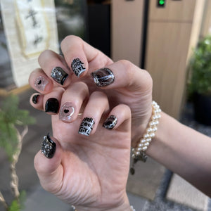 Close-up of a hand with variously designed nails, including text and patterns, with a blurred background.