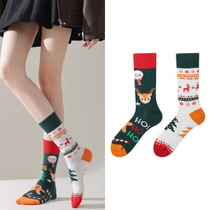 Person wearing festive patterned socks with Christmas designs, including reindeer and snowmen, on a plain background.