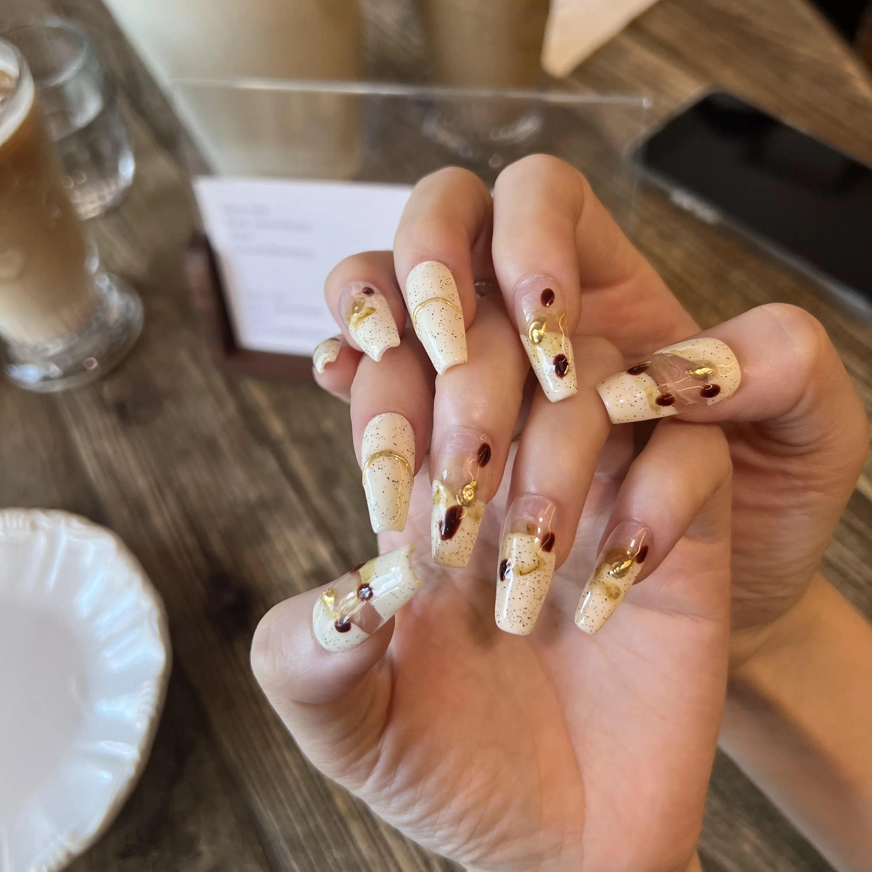 Hand with decorative nail art holding a cup of coffee on a wooden table.