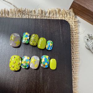 A set of neon green and glittery press on toenails with star, leopard, and chunky sequin designs, displayed on a black board.
