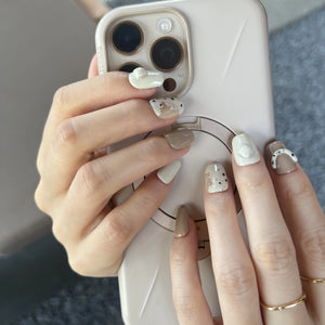 A set of nude and cream press on nails with 3D curved accents and speckled designs, displayed in a wooden tray.