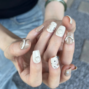 A set of nude and cream press on nails with 3D curved accents and speckled designs, displayed in a wooden tray.