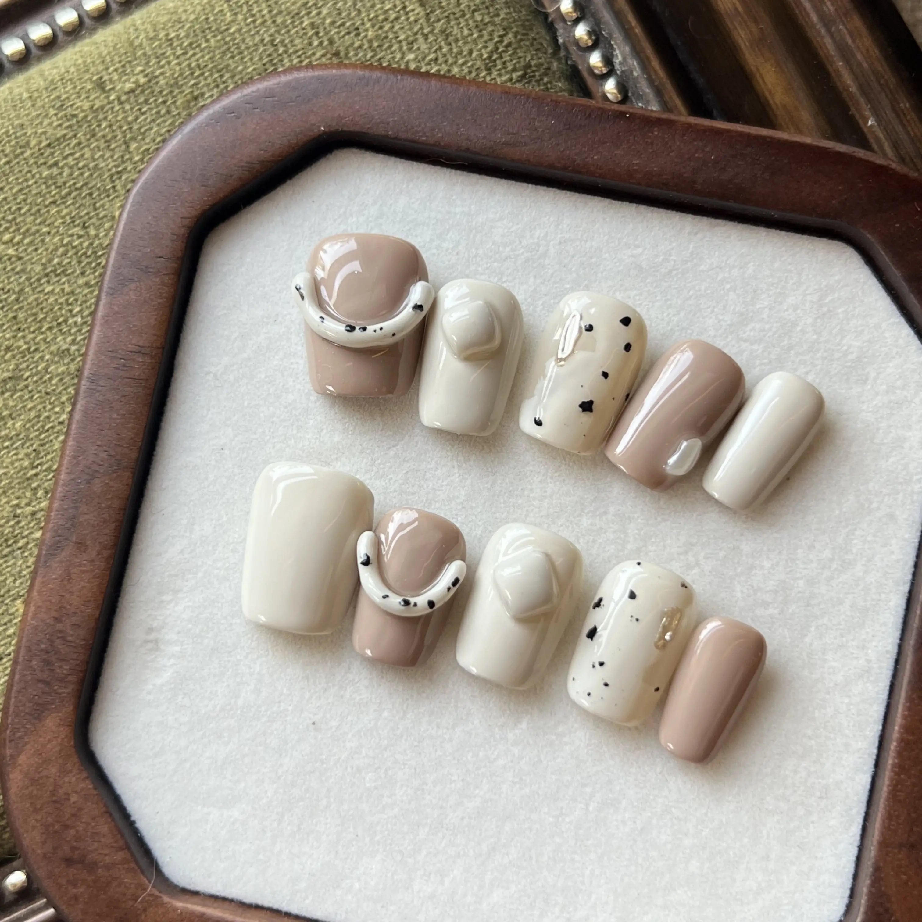 A set of nude and cream press on nails with 3D curved accents and speckled designs, displayed in a wooden tray.