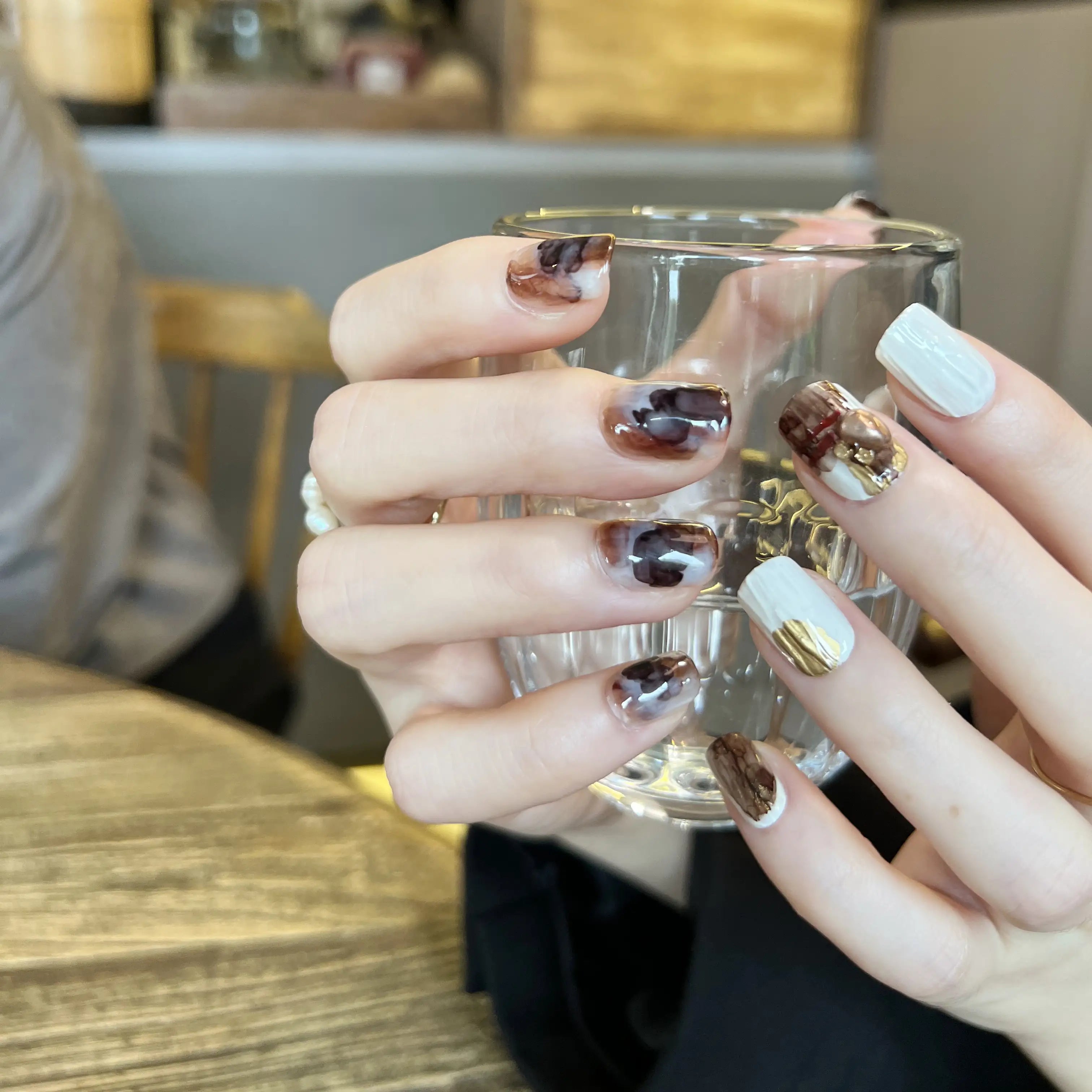 A set of press on nails in marble mocha, creamy white, and gold foil, featuring cable-knit texture and glossy finish, displayed on a card.