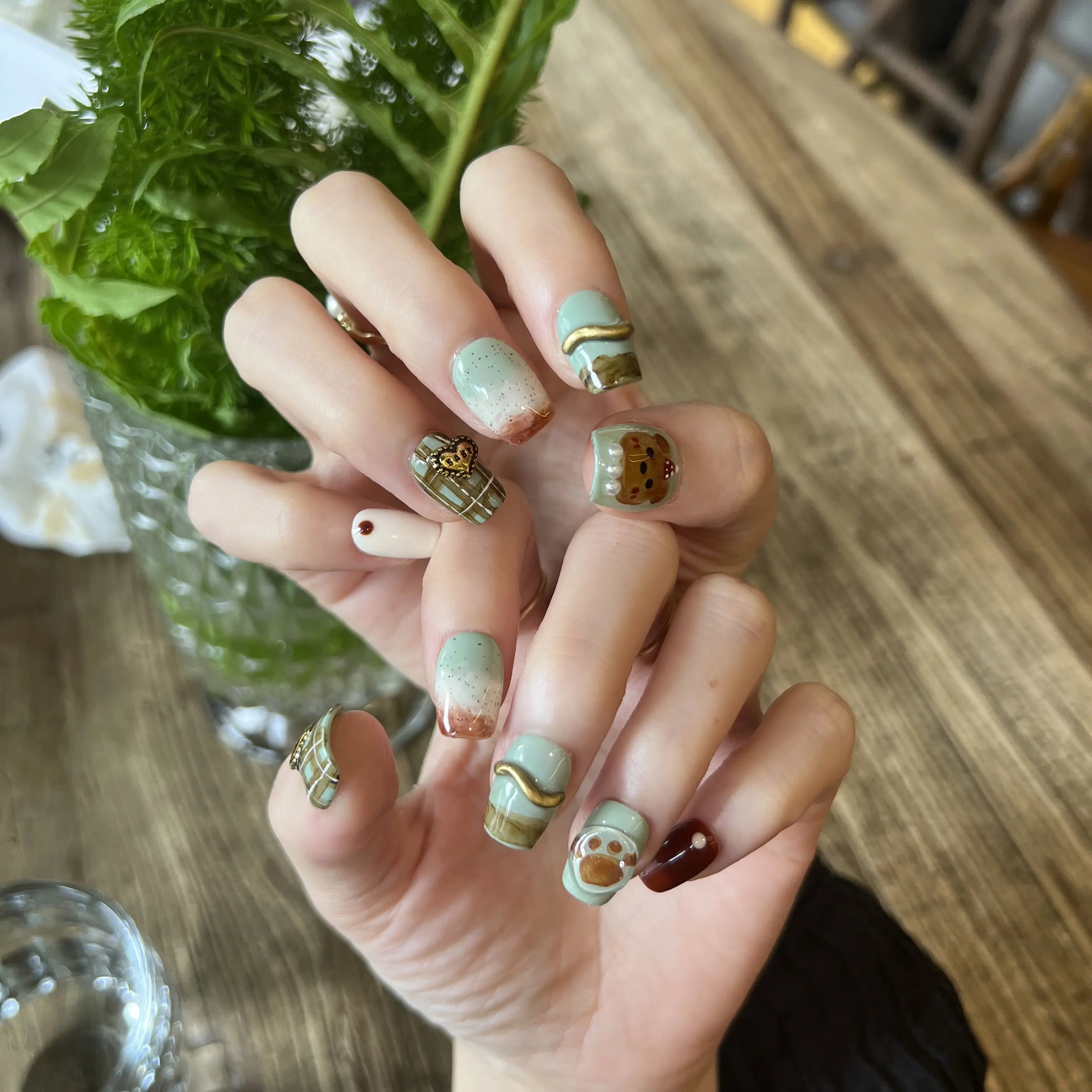Hand with decorative nail art holding a green leafy vegetable on a wooden table.