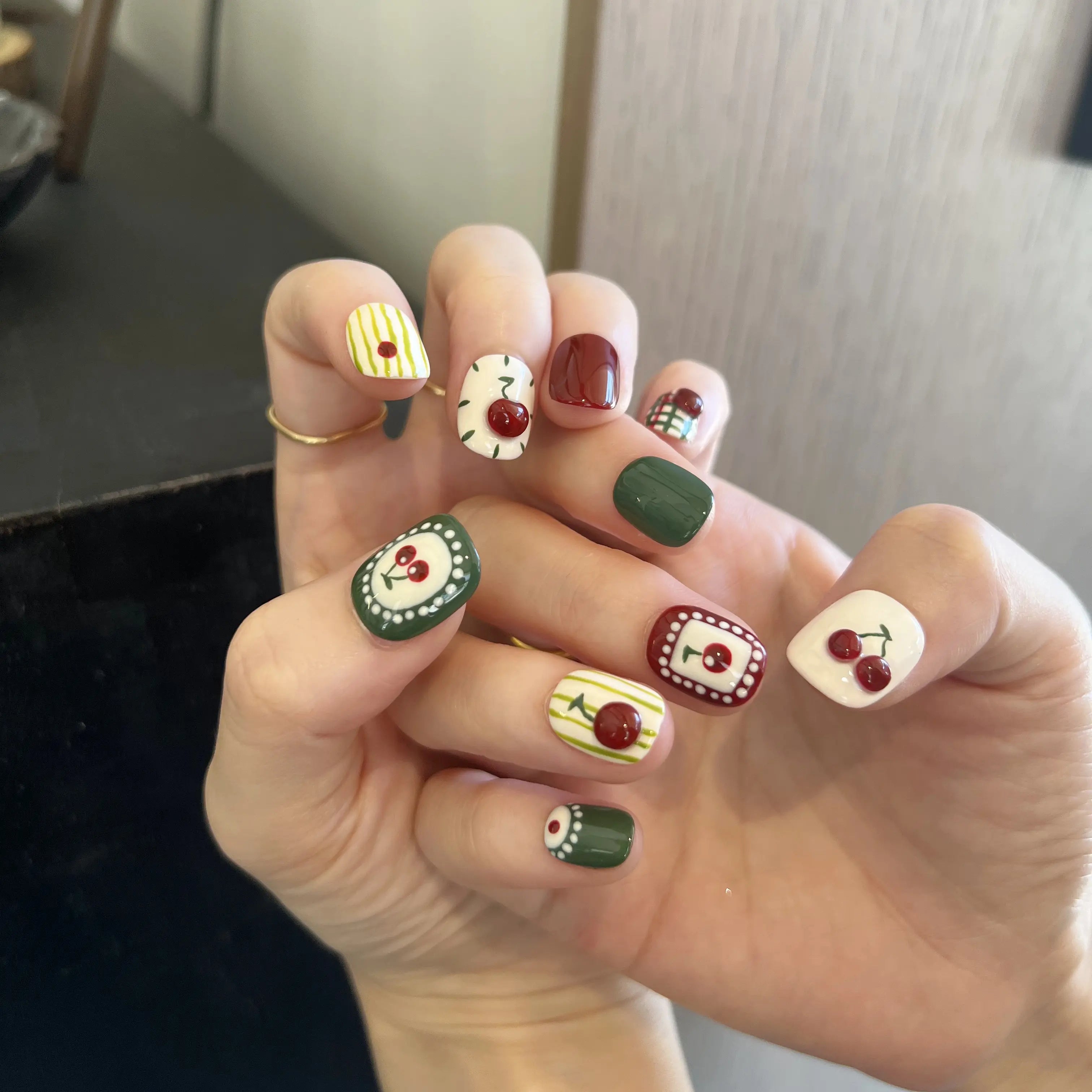 Hand with creatively designed nails featuring cherries and other patterns.