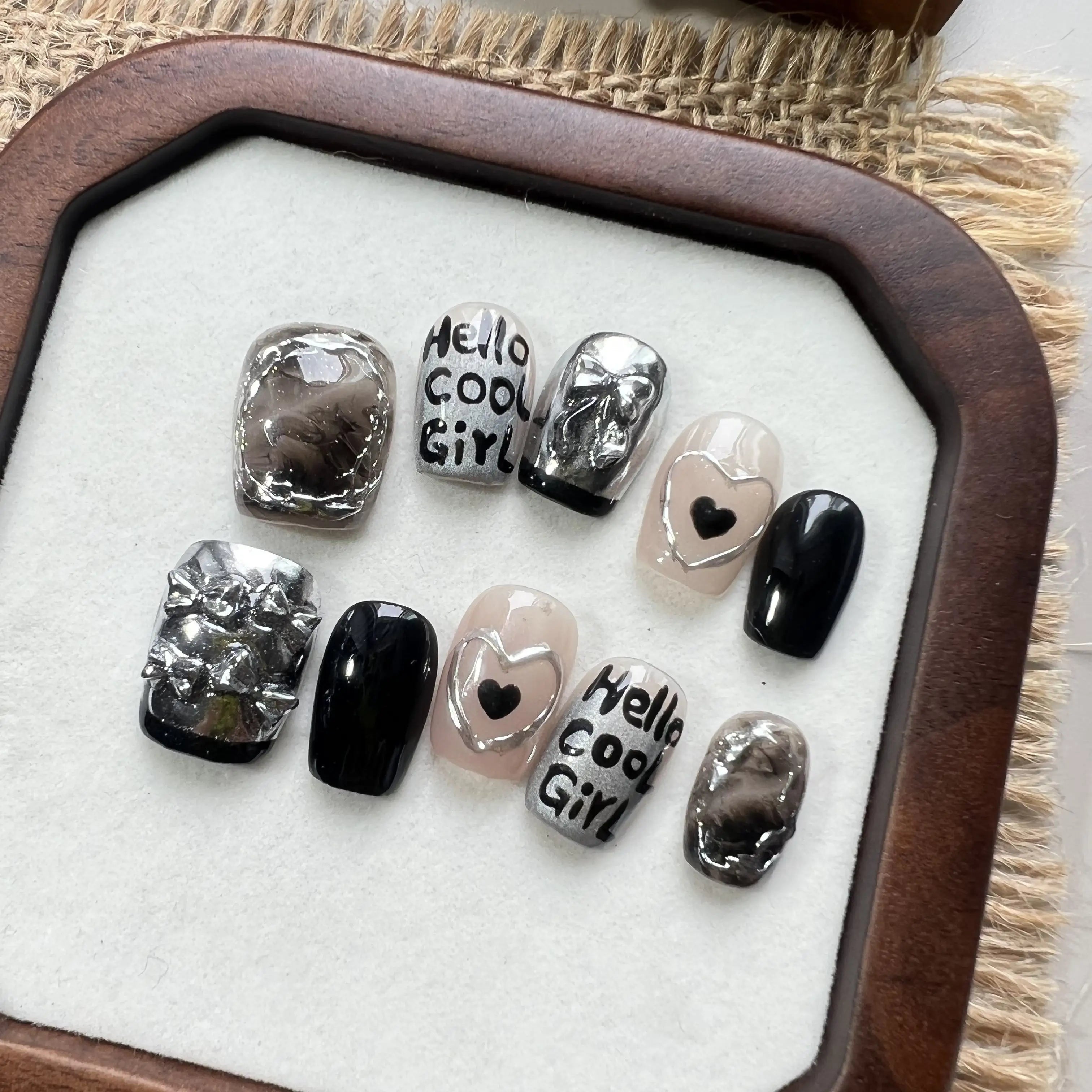 Set of nail art designs on a white surface with a wooden frame, featuring text and heart shapes.
